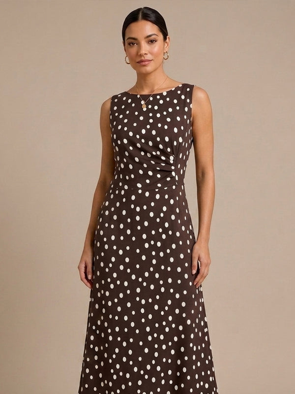 A woman modeling a sleeveless brown maxi dress with a white polka dot pattern against a solid beige studio background.